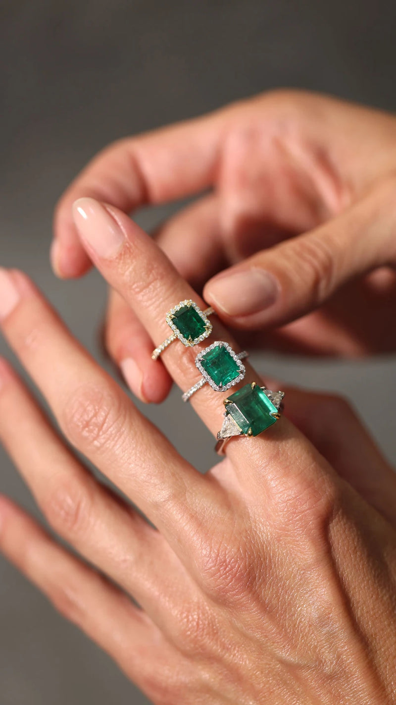 Emerald and diamond engagement rings on a woman's hand.