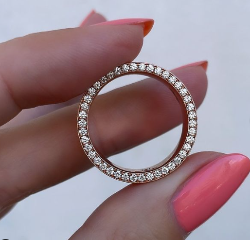 A woman's hand with pink nails holds a men's diamond wedding eternity ring.