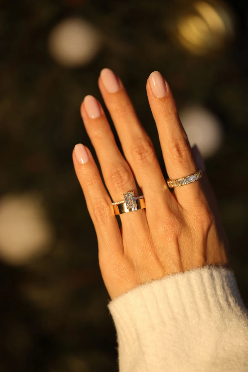 A woman's hand wearing an emerald cut engagement ring paired with a gold wedding band and yellow gold eternity band.
