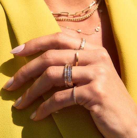 A woman in a bright yellow jacket is wearing stacked diamond eternity bands with different types of diamond settings.