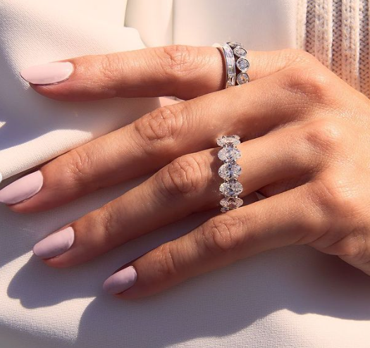 A woman in a white dress wears three diamond eternity rings.
