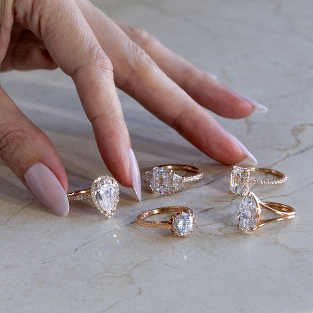 A woman places several Lab Grown Diamond Engagement Rings in Rose Gold on a marble surface. Lab Grown Diamonds do not degrade over time.