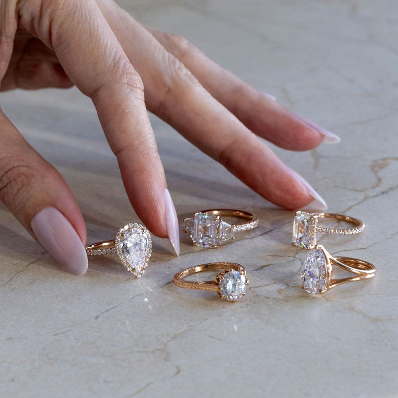 A woman places several Lab Grown Diamond Engagement Rings in Rose Gold on a marble surface. Lab Grown Diamonds do not degrade over time.