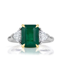 Three carat emerald cut emerald ring with one trillion cut diamond on the left and right of the stone. 