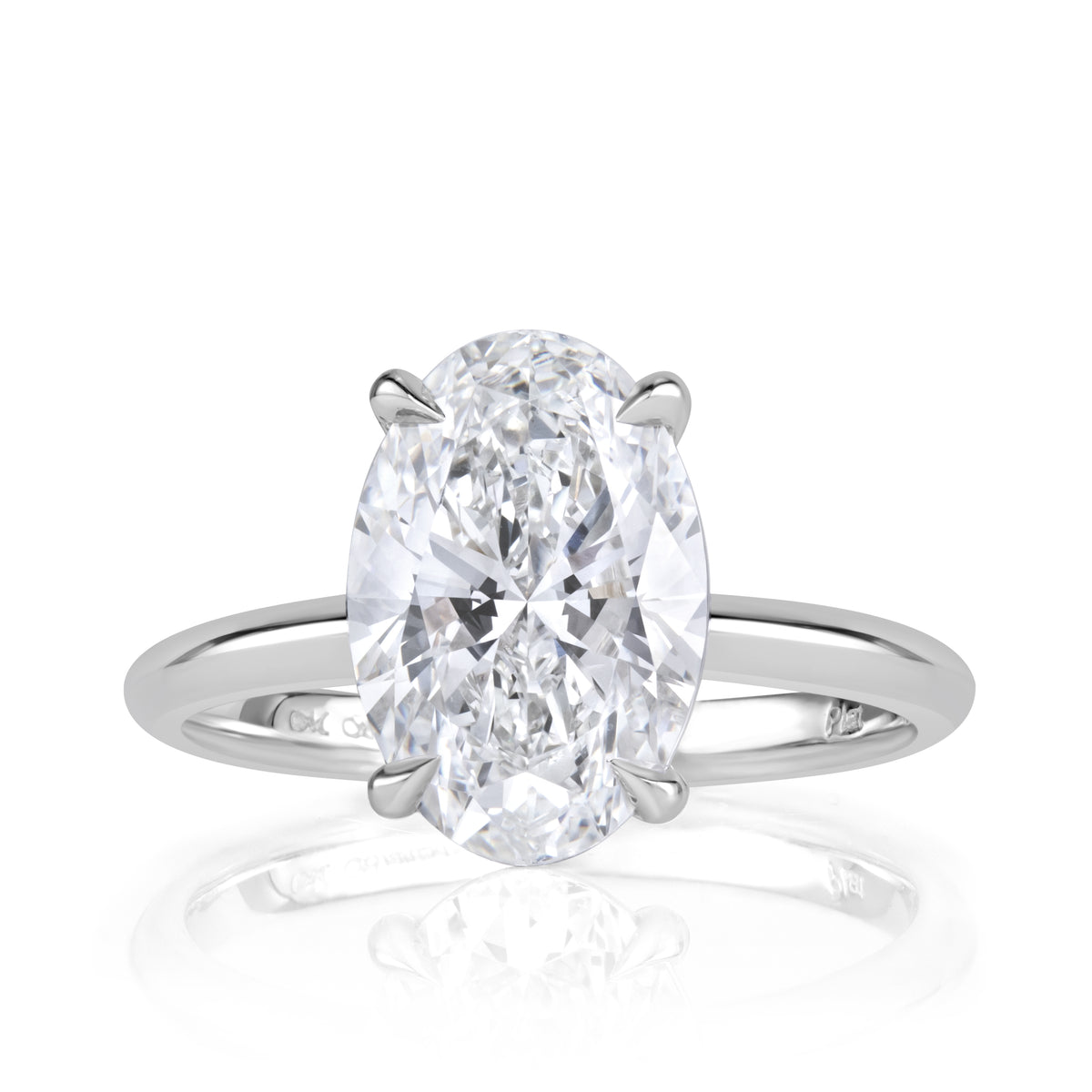 An oval-cut diamond engagement ring in a four-prong setting on a polished silver-colored band, shown against a clean white background with a soft reflection below.
